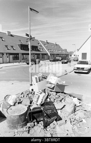 Déchets volumineux dans Overbos Garbage Hoofddorp Nederland, Whizgle News, Dutch Desk, pays-Bas, 1950 - 2000 le 03-08-1988. Ces rubriques sont illustrées dans l'image. La scène capture un coin de rue urbain caractérisé par un mélange de structures résidentielles et de désordre. D'un côté, les maisons soigneusement agencées avec des toits inclinés présentent un aspect uniforme ; leurs façades sont ornées de couleurs sourdes, principalement des nuances de gris et de beige. Chaque bâtiment a une allée ou une petite cour avant, contribuant à un sentiment de vie de banlieue. Au premier plan, un tas de débris perturbe l'atmos autrement ordonné Banque D'Images