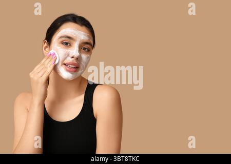 Belle jeune femme enlevant le masque facial avec un tampon de coton sur fond de couleur Banque D'Images