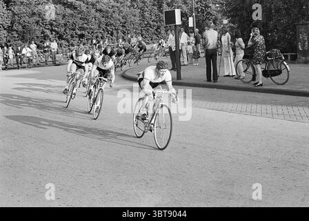 Cyclisme Bennebroek Cycling, Whizgle News, Dutch Desk, pays-Bas, 1950 - 2000 on 10-06-1969. L'image montre ces rubriques. Dans un cadre extérieur animé, un groupe de cyclistes est capturé en mouvement, montrant leur énergie dynamique sur une piste sinueuse. Les cyclistes portent des uniformes assortis de l’équipe, principalement blancs avec des rayures audacieuses, ce qui leur permet de se démarquer sur la surface asphaltée. Leurs corps se penchent vers l'avant, se concentrant intensément alors qu'ils pédalent vigoureusement, avec un cycliste visiblement prenant la tête, faisant preuve de détermination et de concentration. En arrière-plan, il y a une petite foule d’onlooke Banque D'Images