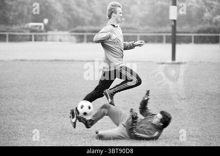 Louis van Gaal nouveau joueur Telstar : Training Football Telstar, Whizgle News, Dutch Desk, pays-Bas, 1950 - 2000 sur 06-09-1977. L'image inclut ces rubriques. Dans un cadre herbeux, deux individus sont engagés dans un moment dynamique d'un match de football. Un joueur, avec des cheveux courts et clairs et portant une veste légère, est capturé en plein air, sautant au-dessus d'un autre joueur qui est au sol. Ce dernier, vêtu d'une tenue plus sombre, semble être dans la position d'un gardien de but, ayant juste tenté d'arrêter un ballon de football qui repose à proximité. La scène transmet une sensation de mouvement et d'intensité, mettant en évidence Banque D'Images