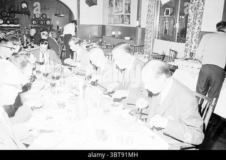 Visitez verre soufflage verre vitrail soufflage verre en général, Whizgle News, Dutch Desk, pays-Bas, 1950 - 2000 le 14-06-1967. Ces rubriques apparaissent dans l'image. Dans un cadre de salle à manger chaleureusement éclairé, un groupe d'hommes est réuni autour d'une longue table, engagé dans un repas. La table est ornée de nappes à carreaux, créant une atmosphère classique et accueillante. Les individus assis ont une gamme de coiffures, avec la plupart des costumes d'affaires sportifs, indiquant une occasion formelle. Leurs expressions varient ; certains sont concentrés sur leurs assiettes, tandis que d'autres semblent être en conversation, ajoutant un sens de came Banque D'Images