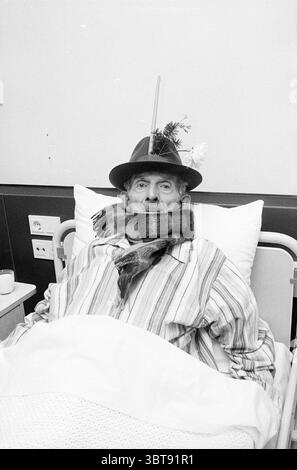 Déménagement de la Croix-Rouge à Beverwijk Relocation, Whizgle News, Dutch Desk, pays-Bas, 1950 - 2000 on 17-12-1973. Ces rubriques sont illustrées dans l'image. Dans la scène, un homme âgé se repose dans un lit d'hôpital, entouré d'un environnement stérile et clinique. Sa tenue se compose d'une chemise rayée qui apporte un sentiment de confort et de familiarité contre les draps blancs durs. Une écharpe épaisse et confortable s'enroule autour de son cou, lui apportant chaleur et touche de personnalité. Il porte un chapeau sombre à larges bords qui se trouve légèrement de travers sur sa tête, ajoutant un caractère fantaisiste à son apparence. Au sommet Banque D'Images