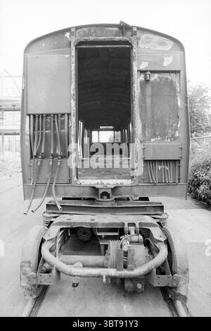 Burned Out metros NS Workshop, Whizgle News, Dutch Desk, pays-Bas, 1950 - 2000 le 02-06-1993. Voici les rubriques de l'image. La scène met en scène un vieux wagon abîmé, positionné bien en vue avec sa porte ouverte face au spectateur. La structure est principalement d'un gris terne et rouillé, avec des taches de peinture écaillée qui font allusion à son âge et à son éclat antérieur. Les tuyaux et les fils métalliques pendent lâchement des côtés exposés, ajoutant une sensation industrielle. L'arrière-plan révèle un aperçu flou d'une zone de construction, avec des cadres squelettiques de bâtiments voisins partiellement obscurcis par le feuillage. Th Banque D'Images