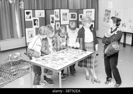 Exposition + discussion des étudiants de Haarlem discussion expositions Haarlem pays-Bas, Whizgle News, Dutch Desk, pays-Bas, 1950 - 2000 le 04-05-1983. Ces rubriques apparaissent dans l'image. Dans un espace intérieur bien éclairé, un groupe de six individus est réuni autour d’une grande table remplie de photographies variées. Le tableau semble encombré mais organisé, présentant un mélange d'images en noir et blanc et en couleur, représentant peut-être des événements ou des personnes importantes pour le groupe. Les personnes debout autour de la table comprennent cinq enfants, qui sont habillés dans des vêtements décontractés et colorés. Ils se penchent Banque D'Images