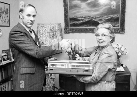 Présentation de la vidéo à MRS Spoelstra IJmuiden Haarlems Dagblad etc. et IJmuider courant et Koeri cérémonie de remise des prix IJmuiden pays-Bas, Whizgle News, Dutch Desk, pays-Bas, 1950 - 2000 on 13-01-1984. Ces rubriques apparaissent dans l'image. La scène capture un moment d'interaction entre deux individus dans un cadre chaleureux et chaleureux. Sur la gauche, un homme en costume formel, avec les cheveux soigneusement peignés et un léger sourire, tend la main pour une poignée de main. Il a un comportement sérieux mais amical, suggérant un sens de formalité dans l'occasion. En face de lui, une femme aux cheveux bouclés, coiffés et Banque D'Images