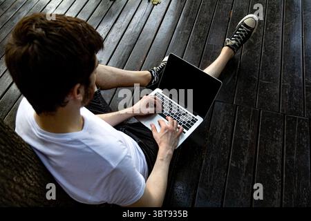 Vue de haut en bas au-dessus de l'épaule d'un homme travaillant sur un ordinateur portable à l'extérieur. L'écran est clairement visible avec un espace pour l'image personnalisée. Banque D'Images