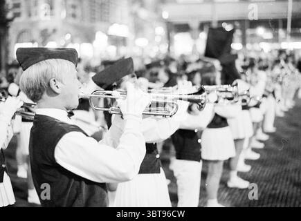 Compétitions de marche Grote Markt Grote Markt Music Haarlem Grote Markt pays-Bas, Whizgle News, Dutch Desk, pays-Bas, 1950 - 2000 le 13-09-1969. L'image montre ces rubriques. La scène capture un défilé nocturne animé, avec un accent central sur un groupe de musiciens au premier plan. Les musiciens portent des gilets sombres sur des chemises blanches, complétés par des casquettes distinctes, qui donnent un sentiment d'uniformité. Leurs visages sont éclairés par les lumières environnantes ambiantes, reflétant la concentration et la fierté pendant qu'ils exécutent. Au premier plan, un musicien se démarque, apportant la trompette à son Li Banque D'Images