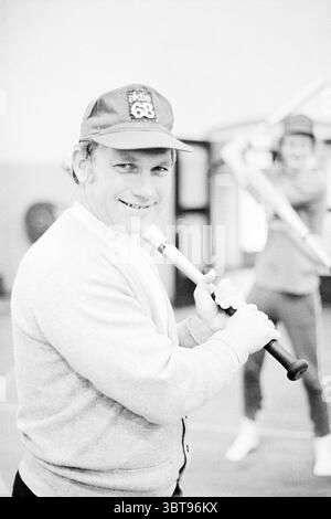 Entraîneur Kinny action '68 Baseball, Whizgle News, Dutch Desk, pays-Bas, 1950 - 2000 on 15-12-1974. Voici les rubriques de l'image. Dans un environnement sportif, un homme se tient debout avec confiance, tenant une batte de baseball. Il a un sourire amical et porte un cardigan gris clair sur une chemise à col, surmonté d'une casquette qui a un logo ou un numéro dessus. La casquette ajoute une touche de couleur à sa tenue autrement neutre. En arrière-plan, une seconde personne est partiellement visible, tenant également une chauve-souris et semblant être en mouvement, suggérant un environnement actif. Les couleurs de la scène sont douces et monochromatiques, Banque D'Images