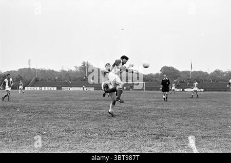 EDO - PEC Football, Whizgle News, Dutch Desk, pays-Bas, 1950 - 2000 sur 05-06-1963. Ces rubriques apparaissent dans l'image. La scène capture un moment dynamique sur un terrain de football gazonné, où deux joueurs sont engagés dans un défi aérien intense pour le ballon. Le joueur au premier plan, vêtu d'un maillot de couleur claire, saute les bras tendus tout en essayant de prendre la tête du ballon. Son expression véhicule détermination et concentration. Le joueur adverse, portant des couleurs plus sombres, est positionné en dessous de lui, atteignant également le ballon avec un regard de concentration. Le ciel est couvert, jetant un gra Banque D'Images