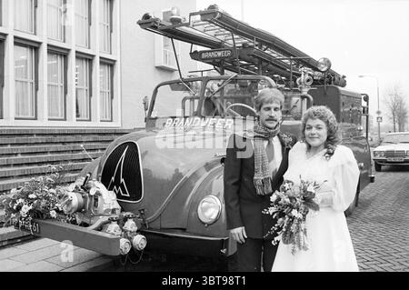Mariage de Mr. Michel avec le vieux pompier IJm. Mariage IJmuiden pays-Bas, Whizgle News, Dutch Desk, pays-Bas, 1950 - 2000 le 16-12-1983. L'image montre ces rubriques. La scène capture un moment de célébration devant un camion de pompiers vintage. Le cadre est urbain, probablement à l'extérieur d'un bâtiment municipal, avec une toile de fond texturée de formations carrées en pierre et de grandes fenêtres rectangulaires. Au premier plan, un couple se tient côte à côte, exsudant joie et excitation. Le marié, vêtu d'un costume sombre avec une chemise de couleur claire et une cravate frappante, a une coiffure classique qui ajoute à la Banque D'Images