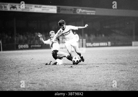 Telstar - Veendam Football Telstar, Whizgle News, Dutch Desk, pays-Bas, 1950 - 2000 on 15-12-1985. L'image montre ces rubriques. La scène capture un moment intense dans un match de football, dans l'ambiance sombre et éclairée d'un stade. Le ciel sombre au-dessus du ciel contraste fortement avec les projecteurs lumineux qui éclairent le champ, créant une atmosphère dramatique. Au premier plan, deux joueurs sont engagés dans une lutte acharnée pour le ballon. Un joueur, vêtu d'un uniforme clair, est légèrement penché en avant, montrant un sentiment de détermination et d'effort alors qu'il tente de prendre le contrôle du Banque D'Images