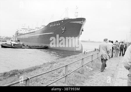 Navire athwart the North Sea canal IJmuiden Ships IJmuiden the Netherlands, Whizgle News, Dutch Desk, the Netherlands, 1950 - 2000 on 12-05-1983. Ce sont les éléments de l'image. La scène montre un grand cargo appelé Belstar, qui attire l'attention avec sa présence imposante. La proue du navire est pointue et conçue pour une navigation efficace, peinte dans une couleur sombre qui contraste avec les teintes plus claires de l'environnement environnant. Au premier plan, un groupe de personnes est rassemblé le long d'un chemin pavé. Ils semblent observer le navire, certains pointant vers lui, suggérant curi Banque D'Images