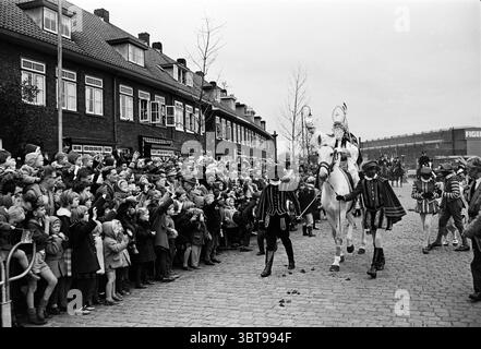 Arrival of Sinterklaas in Haarlem préparé Nicholas Sinterklaas, Whizgle News, Dutch Desk, The Netherlands, 1950 - 2000 on 18-11-1961. L'image montre ces rubriques. La scène est animée d'énergie dans un cadre de rue animé, où une grande foule d'enfants et d'adultes regardent avec impatience une procession. L'atmosphère est remplie d'excitation, soulignée par les expressions joyeuses sur les visages des enfants, dont beaucoup tendent la main avec les bras tendus, leurs visages éclairés avec anticipation. Au premier plan, deux personnages élégamment habillés à cheval sont en évidence. Le cheval est orné de décor Banque D'Images