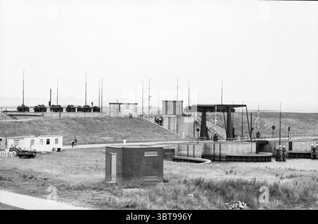 Ecluse Complex à Groningen près de la mer des Wadden, Whizgle News, Dutch Desk, pays-Bas, 1950 - 2000 on 07-1981. Ce sont les éléments de l'image. La scène représente un paysage industriel caractérisé par une série de structures mécaniques et d'infrastructures. En arrière-plan, une série de tours de contrôle hautes et minces s'élèvent au-dessus du paysage, chacune équipée de nombreuses antennes, suggérant une focalisation sur la communication et la surveillance. Les tours sont construites à partir d'un matériau utilitaire, peut-être en métal ou en béton, et leurs surfaces semblent altérées, laissant entendre des années d'exposition à l'ele Banque D'Images