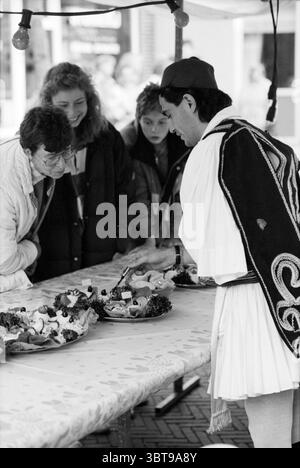 Midsummer festival Hillegom, Whizgle News, Dutch Desk, pays-Bas, 1950 - 2000 le 26-06-1991. L'image montre ces rubriques. Dans un cadre extérieur animé, une scène de marché dynamique se déploie sous un auvent, créant une atmosphère accueillante. Une longue table drapée d'une nappe blanche présente un éventail de plats colorés, garnis d'herbes fraîches et disposés habilement sur des plateaux. Les gens se rassemblent autour de la table, leurs expressions un mélange de curiosité et de plaisir pendant qu'ils examinent la nourriture. Un homme se tient debout à la table, vêtu d'une tenue traditionnelle, avec une cape brodée distinctive et Banque D'Images