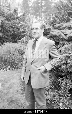 Dean Schonenberg Noordwijkerhout Église catholique romaine religion Noordwijkerhout, Whizgle News, Dutch Desk, pays-Bas, 1950 - 2000 on 29-05-1984. Ces rubriques apparaissent dans l'image. Dans un cadre extérieur serein, un homme d'âge moyen se tient confiant avec un léger sourire. Il est habillé d'un costume de couleur claire avec un motif à carreaux subtil, qui ajoute une touche de sophistication à son apparence. Le tissu du costume reflète un style classique, complété par une cravate rayée soigneusement nouée qui incorpore des nuances de bleu et de marron. La toile de fond est luxuriante et vibrante, remplie de différentes nuances de vert Banque D'Images