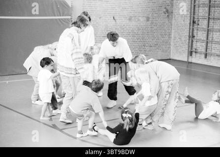 Joke Somers salle de sport pour tout-petits B'dorp Badhoevedorp, Whizgle News, Dutch Desk, pays-Bas, 1950 - 2000 on 20-05-1991. Ces rubriques sont illustrées dans l'image. Dans un gymnase spacieux avec un plancher en bois poli et des murs de briques rouges, une scène animée se déroule. L'atmosphère est remplie d'énergie et d'excitation alors qu'un groupe d'enfants et d'adultes s'engagent dans des activités ludiques. Les individus sont habillés dans un mélange de vêtements décontractés ; certains portent des t-shirts et des shorts colorés, tandis que d'autres sont en survêtement ample. Les enfants, un mélange de garçons et de filles, présentent diverses expressions de plaisir et de concentration Banque D'Images
