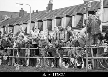 Entrée à Sint IJmuiden IJmuiden pays-Bas, Whizgle News, Dutch Desk, pays-Bas, 1950 - 2000 on 20-11-1992. Voici les rubriques de l'image. La scène est animée de vie, représentant un grand groupe de personnes rassemblées le long d'une clôture. De nombreuses personnes, adultes et enfants, se tiennent debout sur leurs orteils ou se penchent en avant, désireuses d'apercevoir ce qui se passe devant. La foule est diversifiée, avec des enfants en évidence, certains étant tenus par des adultes, mettant en valeur une atmosphère familiale. Le cadre semble être un environnement urbain, indiqué par les bâtiments bordés en arrière-plan, chacun d'eux Banque D'Images