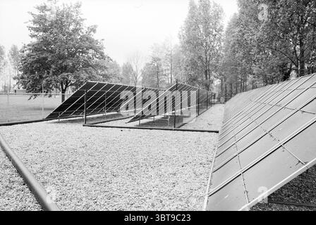 Capteurs solaires piscine Zwanenburg Zonnen Zwanenburg, Whizgle News, Dutch Desk, pays-Bas, 1950 - 2000 le 21-05-1987. L'image inclut ces rubriques. La scène présente une série de grands panneaux inclinés disposés en rangées ordonnées, probablement des panneaux solaires, scintillant dans une lumière douce et diffuse qui suggère un ciel couvert. La structure des panneaux crée un motif géométrique, contrastant avec la douceur naturelle du paysage environnant. Entourant les panneaux, des taches de gravier recouvrent le sol, offrant une base texturée qui complète les surfaces lisses des panneaux. Vege clairsemé Banque D'Images