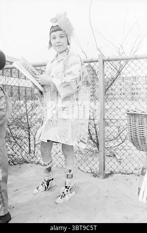 Défilé Schalkwijk parades, Whizgle News, Dutch Desk, pays-Bas, 1950 - 2000 on 01-05-1967. Voici les rubriques de l'image. Dans la scène, un jeune se tient confiant contre une clôture à maillons de chaîne, exsudant une ambiance ludique et fantaisiste. Ils sont habillés dans une tenue créative faite principalement de journaux, qui forme un manteau de fortune unique qui drape librement. Le manteau est orné de divers motifs imprimés en noir et blanc qui ajoutent de la texture et de l'intérêt. L'individu arbore un casque vibrant, avec un arc ou une fleur surdimensionné, ajoutant une touche de contraste contre le t discret Banque D'Images