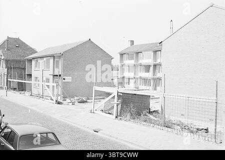 Nouvelle construction Bennebroek construction construction Pits, Whizgle News, Dutch Desk, pays-Bas, 1950 - 2000 le 08-09-1969. Voici les rubriques de l'image. La scène représente une zone de construction adjacente à une rue résidentielle. Sur la gauche, une maison pittoresque de deux étages en briques présente une atmosphère chaleureuse, avec son toit en tuiles et une cour modeste. La brique affiche un ton gris clair, contrastant avec les tuiles de toit plus foncées. À côté de cette maison, un bâtiment inachevé se dresse avec des cadres exposés et une façade austère et sans ornement. L'échafaudage longe la structure, faisant allusion aux travaux en cours. Les compos Banque D'Images