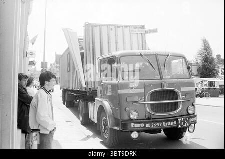 Camion avec conteneur ouvert déchiré à la gare du viaduc ferroviaire Haarlem Jansweg pays-Bas, Whizgle News, Dutch Desk, pays-Bas, 1950 - 2000 on 07-1968. Ces rubriques apparaissent dans l'image. Dans une scène urbaine animée, un vieux camion domine le premier plan, son extérieur altéré présentant des nuances de rouge et de gris profonds, indicatifs de son âge. Le véhicule, équipé d'un conteneur de chargement de grande taille, est stationné parallèlement au trottoir, légèrement incliné pour accueillir son grand cadre. Les embellissements du camion, y compris une calandre avant proéminente et des phares ronds, lui confèrent une allure classique et robuste Banque D'Images
