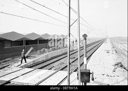 Station de construction Heemskerk construction construction Pits Station, Whizgle News, Dutch Desk, pays-Bas, 1950 - 2000 on 12-05-1969. L'image contient ces rubriques. La scène montre un chantier de construction de chemin de fer avec une vue panoramique sur les lignes de voie qui s'étendent au loin. D'un côté, un travailleur est engagé dans le travail manuel, paraissant concentré alors qu'il navigue dans la zone. Il porte des vêtements typiques pour un tel travail, adaptés à la durabilité et à la sécurité. À gauche, on peut voir une série de structures angulaires, couvertes de briques, leurs lignes pointues et leur uniformité formant un architecte distinct Banque D'Images