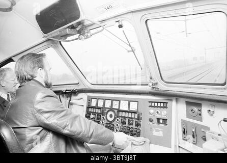 1er train sur les trains de la ligne Schiphol, Whizgle News, Dutch Desk, pays-Bas, 1950 - 2000 le 02-10-1978. L'image montre ces rubriques. La scène capture l’intérieur du cockpit d’un train, mettant en valeur un mélange de design rétro et fonctionnel. Deux personnes sont présentes, dont une assise dans la position du conducteur, contrôlant activement le train. Le conducteur, un homme à la barbe soignée, est habillé d'une veste en cuir foncé qui contraste avec les tons clairs de l'intérieur de l'habitacle. Son attention se concentre sur un éventail de commandes, y compris des leviers et des boutons, qui sont méticuleusement disposés Banque D'Images