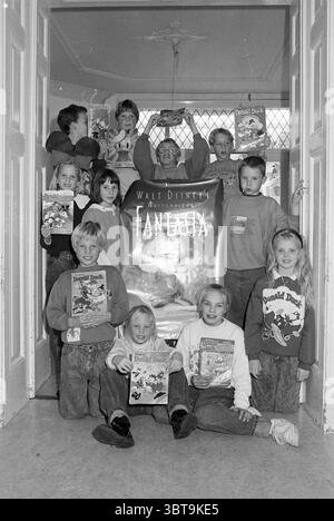 Enfants dus à Donald Duck, Whizgle News, Dutch Desk, pays-Bas, 1950 - 2000 on 15-10-1992. L'image contient ces rubriques. Dans un cadre intérieur animé, un groupe d'enfants est réuni, montrant un sentiment d'excitation et de joie. La lumière filtre à travers une fenêtre, projetant une douce lueur dans tout l'espace, créant une atmosphère accueillante. Il y a une grande affiche bien en vue au centre, représentant une scène fantaisiste qui fait allusion à la fantaisie et à l'imagination. Les enfants, qui varient en âge et en apparence, expriment un éventail d'émotions, allant de larges sourires à des expressions ludiques. Certains tiennent bon Banque D'Images