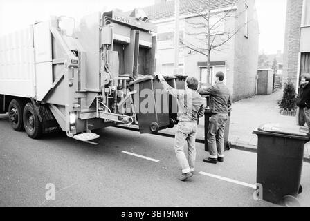 Collecte des seaux à ordures, Whizgle News, Dutch Desk, pays-Bas, 1950 - 2000 sur 19-11-1989. L'image montre ces rubriques. Dans un cadre urbain animé, un camion à ordures est bien en vue, son grand cadre industriel occupant une grande partie de la rue. Le véhicule est peint dans une couleur sourde, peut-être une nuance de gris clair, qui contraste avec l'asphalte plus foncé de la route. L'arrière du chariot est ouvert, révélant un système mécanique conçu pour soulever et vider les poubelles. Deux personnes participent activement au processus. Une personne, vêtue d'une veste en denim et d'un pantalon léger, est positionnée ne Banque D'Images