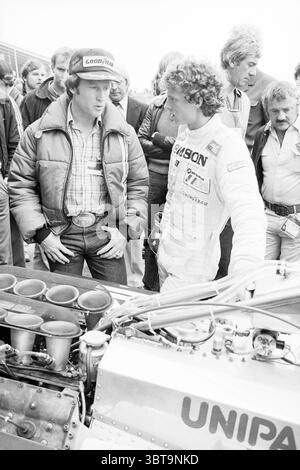 Kenny Roberto et Jan Lammers Grand Prix, Whizgle News, Dutch Desk, pays-Bas, 1950 - 2000 le 29-08-1980. Ce sont les éléments de l'image. La scène capture un moment dans un environnement animé, probablement lors d'un événement de sport automobile. Au premier plan, deux hommes s'engagent dans la conversation et semblent concentrés sur un véhicule mécanique. On est vêtu d'une veste épaisse et sombre et d'une casquette ornée d'un logo, donnant un comportement décontracté mais sérieux. Il se tient debout avec une présence dominante, faisant des gestes pendant qu'il parle. L'autre homme, vêtu d'un costume de course, présente un look de concentration, penchant sl Banque D'Images