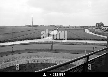 Lieu de construction H + K Velserbroek, Whizgle News, Dutch Desk, pays-Bas, 1950 - 2000 on 10-03-1996. Ces rubriques sont illustrées dans l'image. La scène présente un vaste paysage ouvert caractérisé par des champs étendus et des voies navigables douces. Un ruisseau étroit serpente à travers le terrain herbeux, reflétant le ciel couvert dans sa surface calme. Autour de la voie navigable, une herbe verte luxuriante s'étend, parsemée de taches occasionnelles de fleurs sauvages qui offrent de subtiles notes de couleur contre les tons majoritairement gris. En arrière-plan, une ligne d’arbres marque l’horizon, leurs silhouettes Banque D'Images