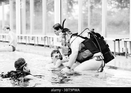 Club de plongée H'stede piscine Heemstede pays-Bas, Whizgle News, Dutch Desk, pays-Bas, 1950 - 2000 le 27-08-1994. L'image contient ces rubriques. Dans un cadre aquatique serein, un groupe d'individus s'engage dans une séance de plongée sous-marine dans une piscine intérieure spacieuse. L'eau est calme, reflétant les plafonniers et créant un effet chatoyant sur les bords carrelés. L'accent est mis principalement sur deux adultes en équipement de plongée, l'un aidant l'autre, qui est légèrement submergé. Les deux portent des masques et des tubas, avec un sens palpable du travail d'équipe évident dans leurs interactions. L'assistance Banque D'Images