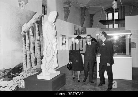 Ouverture de l'exposition Medicine Man ouvertures ouverture commande d'expositions Haarlem Grote Markt pays-Bas, Whizgle News, Dutch Desk, pays-Bas, 1950 - 2000 le 05-04-1972. L'image contient ces rubriques. La scène se déroule dans une galerie d'art caractérisée par de hauts plafonds et de l'espace, avec de la lumière qui pénètre à travers de grandes fenêtres ornées d'une architecture ornée. Les murs présentent des photographies historiques en noir et blanc et des peintures murales représentant d'anciennes colonnes, évoquant un thème de l'histoire classique. Au premier plan, trois individus s'engagent avec une statistique de marbre blanc proéminente Banque D'Images
