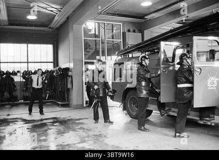 Intérieur du garage des pompiers la brigade des pompiers de Haarlem répond., Whizgle News, Dutch Desk, pays-Bas, 1950 - 2000. L'image contient ces rubriques. Dans une caserne de pompiers spacieuse et bien éclairée, plusieurs personnes sont engagées dans diverses activités. L'intérieur respire un sens de l'ordre, avec des sols brillants reflétant l'éclairage aérien. Le cadre se caractérise par de hauts plafonds et de grandes fenêtres, permettant à la lumière naturelle de se répandre, éclairant la scène. Sur la gauche, un présentoir présente des équipements de lutte contre les incendies soigneusement agencés, y compris des casques et des vestes, suggérant une disponibilité pour l'action. Le co Banque D'Images