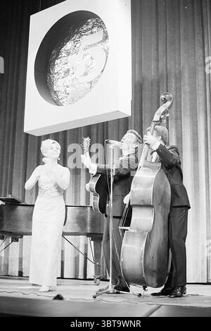 Bergers dans IJmuiden Music, Whizgle News, Dutch Desk, The Netherlands, 1950 - 2000 sur 18-10-1968. L'image contient ces rubriques. Dans un cadre de performance dynamique, trois artistes sont engagés dans un spectacle énergique sur une scène ornée de riches rideaux aux couleurs profondes. La toile de fond présente un cercle proéminent, ajoutant un point focal au-dessus de l'ensemble, et contrastant avec le tissu avec sa simplicité graphique. La figure centrale est une femme, vêtue d'une robe élégante et chatoyante qui reflète les lumières de la scène, créant un effet lumineux. Elle se tient gracieusement, sa posture transmettant les deux Banque D'Images