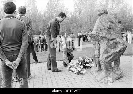 Dépôt de couronnes Nieuw Vennep Remembrance Day, Whizgle News, Dutch Desk, pays-Bas, 1950 - 2000 le 04-05-1984. L'image montre ces rubriques. La scène capture un sombre rassemblement en plein air centré autour d'une statue, qui représente deux personnages engagés dans un moment de contemplation ou de souvenir. La statue est texturée et légèrement altérée, fabriquée à partir de pierre sombre ou de métal, donnant un sentiment de permanence et de gravité à l'atmosphère. Un groupe d'individus se tient à proximité, avec un accent sur deux hommes au premier plan. L'une, vêtue d'une veste légère et de lunettes, se plie légèrement pour placer un bouquet de f Banque D'Images