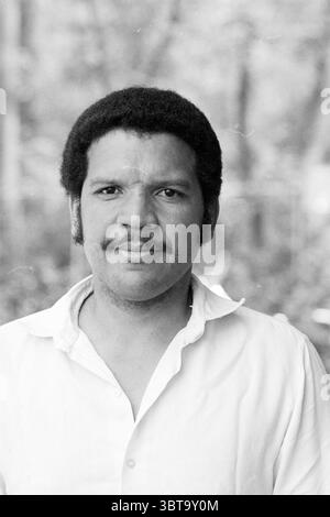 Portraits de joueurs de cricket Bloemendaal Cricket Bloemendaal, Whizgle News, Dutch Desk, pays-Bas, 1950 - 2000 sur 10-05-1981. Ce sont les éléments de l'image. Dans la scène, un homme se tient confiant avec un léger sourire, exsudant chaleur et accessibilité. Il a une tête pleine de cheveux foncés et bouclés, coiffés naturellement, et une moustache proéminente qui complète ses traits du visage. Son expression transmet un sentiment de calme et de facilité. Vêtu d'une chemise boutonnée blanche, le tissu semble doux et légèrement froissé, laissant présager une atmosphère décontractée. La chemise contraste magnifiquement avec sa peau à Banque D'Images