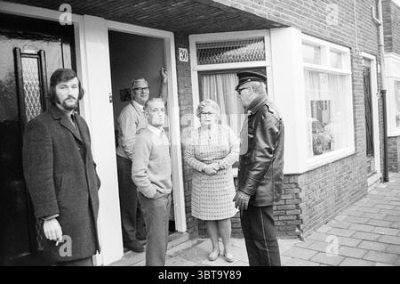 Les résidents protestent contre les bâtiments récréatifs prévus, Whizgle News, Dutch Desk, pays-Bas, 1950 - 2000. L'image montre ces rubriques. Dans un cadre résidentiel pittoresque, un groupe de cinq personnes se tient juste à l'extérieur d'un bâtiment, créant un tableau qui capture un moment d'interaction. La façade du bâtiment est composée de briques durables, avec un mélange de briques apparentes et de garnitures blanches soulignant l'entrée. D'un côté, un homme avec une barbe soigneusement soignée et portant un manteau sombre et texturé se penche avec désinvolture, regardant les autres avec une expression quelque peu sérieuse. A côté de lui, un gentil plus âgé Banque D'Images