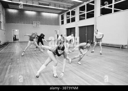 Patineurs d'entraînement patinage sur glace, Whizgle News, Dutch Desk, pays-Bas, 1950 - 2000 le 11-01-1972. L'image montre ces rubriques. Dans un gymnase intérieur spacieux, plusieurs personnes sont engagées dans une activité dynamique, pratiquant probablement un sport ou un exercice physique. Le sol est fait de bois poli, reflétant la lumière ambiante des luminaires suspendus. D’un côté, des gradins en bois sont visibles, suggérant un lieu souvent utilisé pour des événements. Les murs sont peints dans une couleur claire, et de grandes fenêtres permettent à la lumière naturelle de filtrer, créant une atmosphère lumineuse ponctuée d'ombres projetées par le participant Banque D'Images