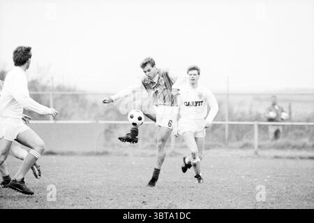 Football Zandvoort '75 Football Zandvoortse Meeuwen Halfweg, Whizgle News, Dutch Desk, pays-Bas, 1950 - 2000 on 05-11-1988. Ces rubriques sont illustrées dans l'image. La scène capture un moment dynamique sur un terrain de football, où trois joueurs sont activement engagés dans le jeu. Le cadre est une arène sportive en plein air, probablement pendant une journée nuageuse, car l'éclairage est doux et diffus, créant une atmosphère quelque peu silencieuse. Au premier plan, un joueur est vu frapper un ballon de football avec précision. Il porte un maillot avec un motif audacieux et le numéro six mis en évidence, contrastant avec une paire Banque D'Images