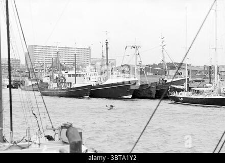 Bateaux de pêche sportive + activistes IJm. Navires pêche et autres poissonniers pêchant IJmuiden pays-Bas, Whizgle News, Dutch Desk, pays-Bas, 1950 - 2000 on 17-12-1979. Ces rubriques apparaissent dans l'image. La scène capture un port animé, mettant en vedette une collection variée de bateaux amarrés près les uns des autres. Chaque navire est distinctif, allant des petits bateaux de pêche aux navires plus grands et plus robustes, leurs coques peintes dans des tons de blanc, noir et gris, créant un contraste frappant avec l'eau ondulée. Les bateaux présentent différentes formes et tailles, indiquant leurs différentes fonctions Banque D'Images