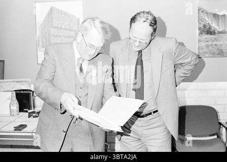 Adieu J. van Rosmalen Spectrum Spectrum, Whizgle News, Dutch Desk, pays-Bas, 1950 - 2000 le 28-05-1982. Ces rubriques apparaissent dans l'image. Dans un cadre intérieur bien éclairé, deux hommes sont engagés dans une discussion ciblée sur un document qu’ils examinent ensemble. Le premier homme, vêtu d'un costume gris avec une médaille épinglée à son revers, a une expression réfléchie en se penchant légèrement en avant, profondément investi dans le contenu du dossier. Il a des cheveux de couleur claire, coiffés soigneusement, et porte des lunettes qui accentuent son comportement attentif. À côté de lui, le deuxième homme est vêtu de façon décontractée d'un c. Banque D'Images