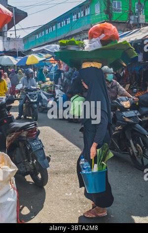Balikpapan, Indonésie - 19 avril 2025. La vendeuse de gado-gado porte ses marchandises sur sa tête et un petit seau tout en marchant vers le marché. Banque D'Images