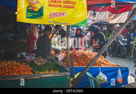 Balikpapan, Indonésie – 19 avril 2025. Un vendeur vend des piments frais et des légumes sur un marché traditionnel animé, tandis que les acheteurs naviguent sous colo Banque D'Images