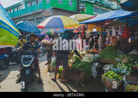 Balikpapan, Indonésie - 19 avril 2025. Scène occupée au marché traditionnel de Pandan Sari avec des gens magasinant pour des légumes frais sous un parapluie coloré Banque D'Images