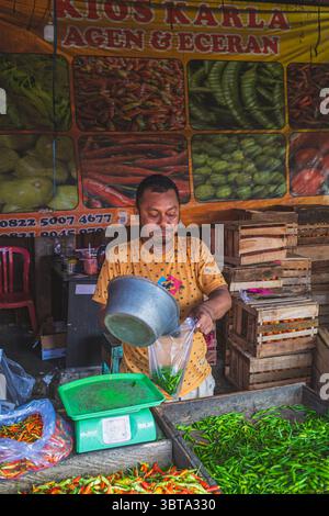 Balikpapan, Indonésie – 19 avril 2025. Un vendeur de marché ramasse les piments verts dans un sac en plastique à un stand d'épices traditionnel. Banque D'Images
