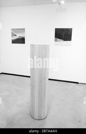 Art Hetty Huisman, Whizgle News, Dutch Desk, pays-Bas, 1950 - 2000 le 15-03-1992. Ces rubriques sont illustrées dans l'image. La scène présente une galerie d'art minimaliste à l'esthétique épurée et moderne. Au premier plan se dresse un piédestal cylindrique en bois de couleur claire, sa surface affichant un grain subtil. La finition lisse du piédestal crée un contraste avec le sol en béton texturé plus rugueux, qui est un ton gris discret. En arrière-plan se trouvent deux œuvres accrochées au mur, chacune présentant des motifs abstraits. One Piece présente un paysage rendu dans des tons doux et discrets Lik Banque D'Images