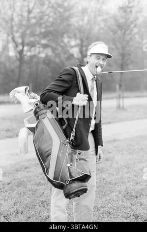 Golfer Hits ball., Whizgle News, Dutch Desk, pays-Bas, 1950 - 2000 sur 10-1988. L'image inclut ces rubriques. La scène capture un jeune homme debout sur une zone herbeuse qui semble faire partie d'un terrain de golf. Il est habillé d'un blazer sur mesure et d'un pantalon de couleur claire, suggérant une approche chic-décontractée ou formelle du golf. Un sac de golf, rempli de clubs, est accroché sur son épaule, et il tient un club de golf dans sa bouche de manière ludique, mettant en valeur un comportement léger. L'homme a les cheveux courts et une casquette qui ajoute une touche sportive à sa tenue. L'arrière-plan présente un paysage flou de Banque D'Images