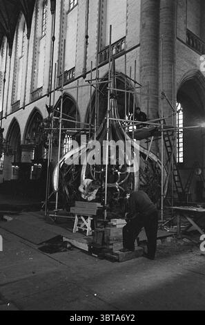 Travail sur l'oignon de la Grote ou Sint-Bavokerk tapant les spinnacles avec le plomb Grote Kerk Haarlem églises produit Bavokerk travail Haarlem Grote Markt pays-Bas, Whizgle News, Dutch Desk, pays-Bas, 1950 - 2000 on 02-02-1965. L'image inclut ces rubriques. La scène capture un moment dans un intérieur spacieux de style gothique, probablement une église ou une cathédrale, caractérisé par ses arches imposantes et ses pierres complexes. Les grandes fenêtres permettent à la lumière douce et diffuse de filtrer, projetant de légères ombres sur les surfaces environnantes. Au centre, un grand lustre orné occupe le premier plan Banque D'Images